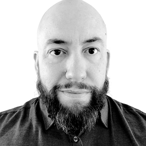 A black and white photo of a bald man with a beard, smiling gently.